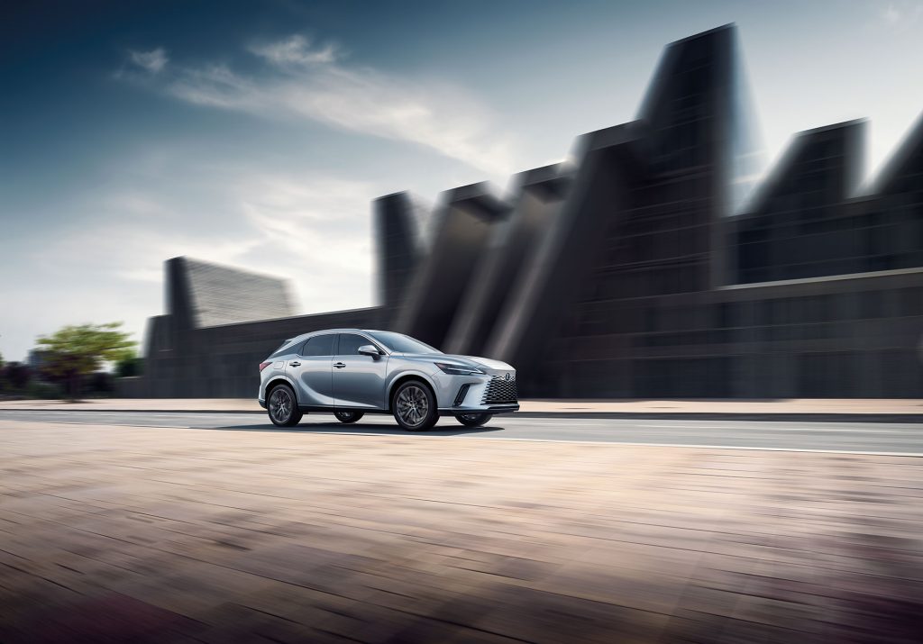 An all new silver 2025 Lexus RX EV driving through a downtown setting. - Lexus of Huntsville, AL