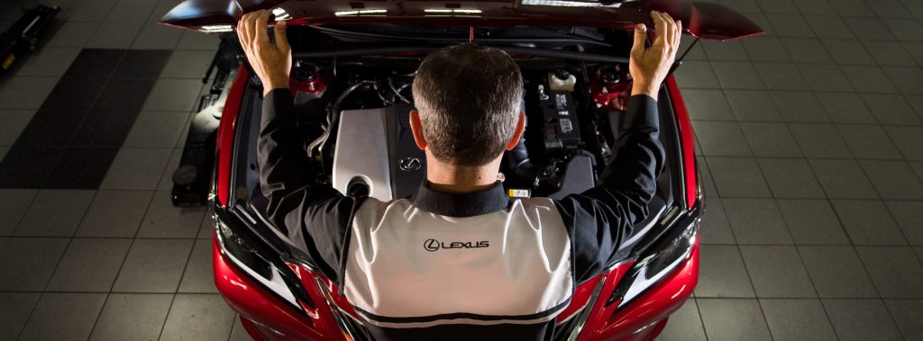 A Lexus certified technician looking under the hood of a red Lexus vehicle. - Lexus of Huntsville, AL